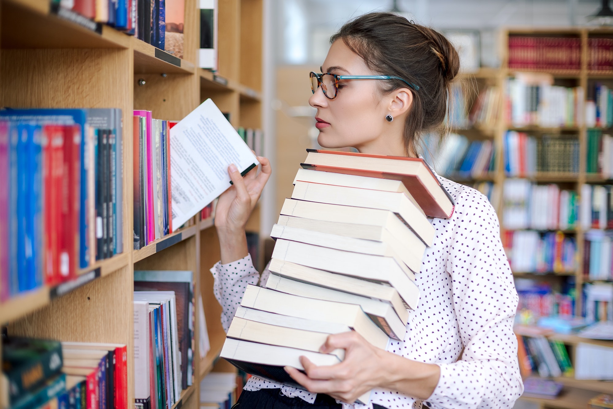 Young woman with a stack of books in library